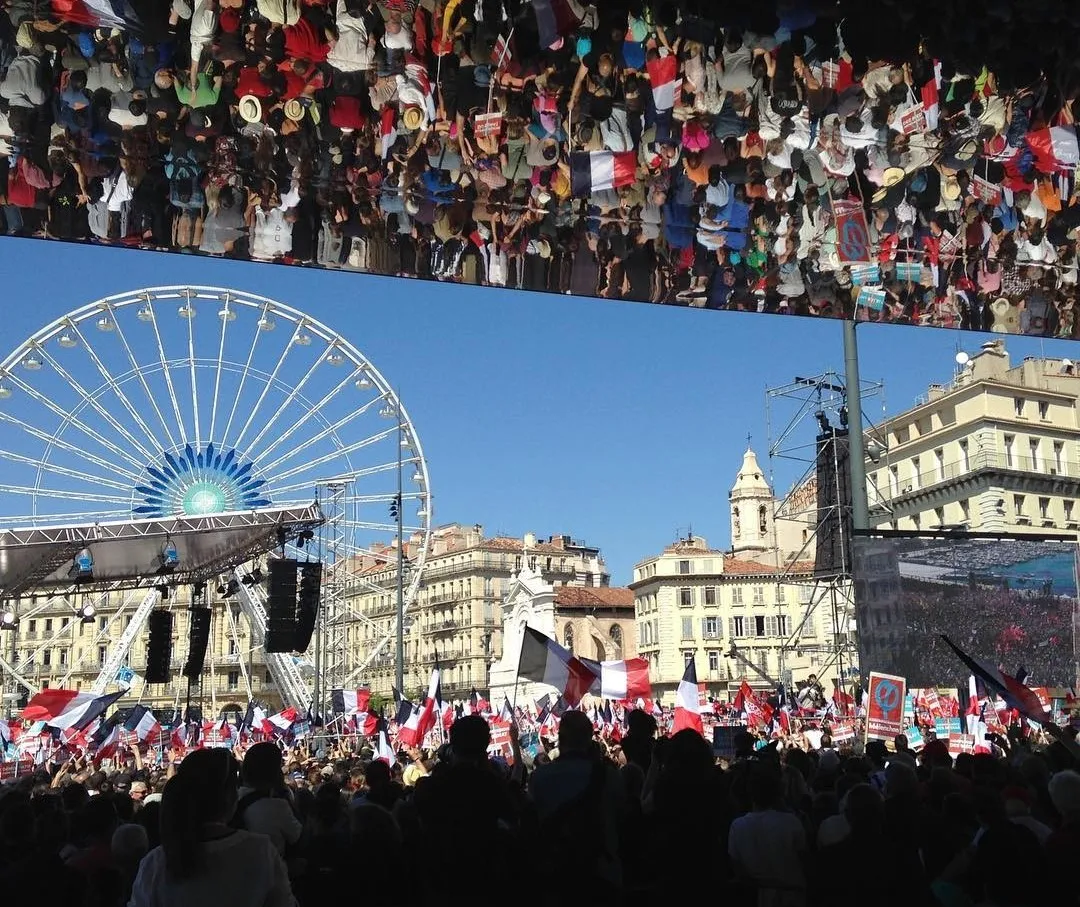 Une foule rassemblée sur le Vieux-Port de Marseille pour un meeting de Jean-Luc Mélenchon, avec une grande roue en arrière-plan.
